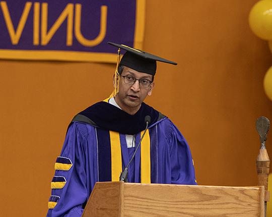 man with robe, glasses, talking at a podium