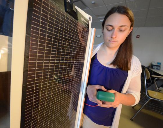 student looking at a multimeter in front of a solar panel